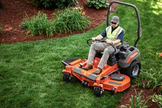 Une personne qui conduit une tondeuse autoportée dans un jardin bien entretenu.