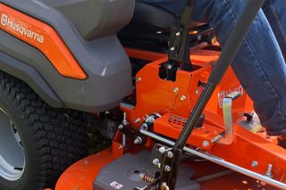 En person som kör en Husqvarna åkgräsklippare på gräs och visar klipparens klippaggregat.