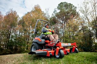 A person operating a ride-on mower on a grassy slope with trees in the background.