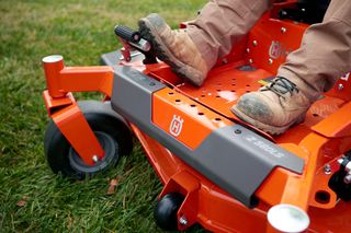 Close-up of a person operating a ride-on lawn mower, focusing on the foot pedal area.