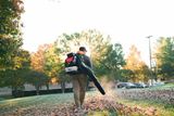 A person using a leaf blower to clear fallen leaves in a park setting.
