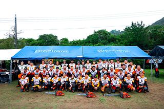 ハスクバーナブランドのテントの下でチェーンソーを持ってポーズをとる作業服を着た人々のグループ。