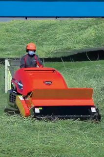 野原で背の高い草を刈る乗用芝刈り機を操作する人。