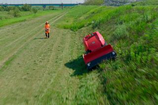 草の斜面を歩く人と、ロボットの芝刈り機が坂道で動いています。