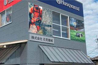 ハスクバーナの建物の外観には、大きな看板とチェーンソーを使用している人の画像があります。