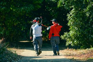 園芸道具を背負って林道を歩く2人。