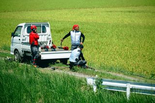 畑で3人の労働者が、農作業のためにトラックから機器を準備しています。